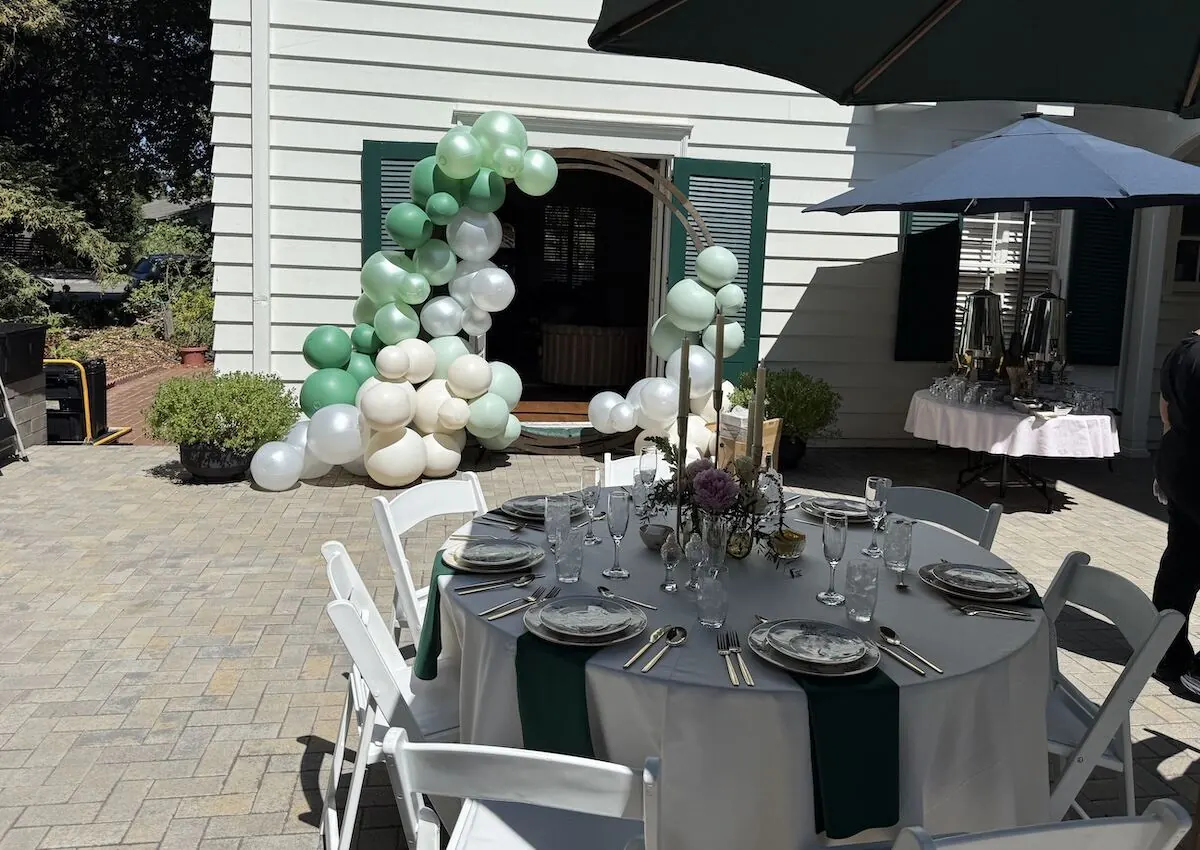 Sage and ivory balloon garland arcing over a doorway beside a fully styled table — balloon and bloom styling from SF catering