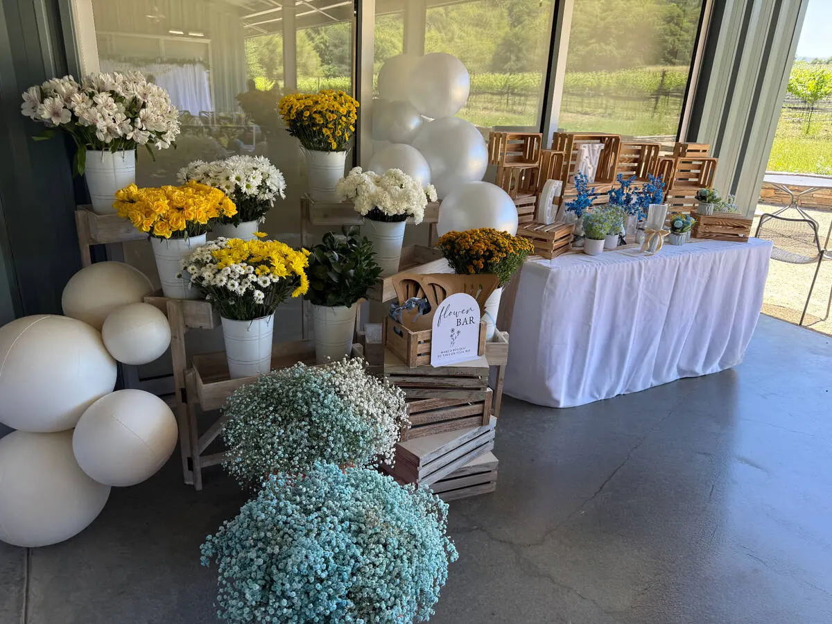 Guest-serve bloom bar stocked with yellow roses, daisies and baby's breath alongside wrapping paper and ribbon — signature bloom bar from San Francisco and Brisbane catering