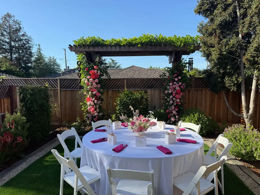 Rose arch shading a garden round finished in crisp white cloth with fuchsia napkins — bespoke floral installations from San Francisco catering